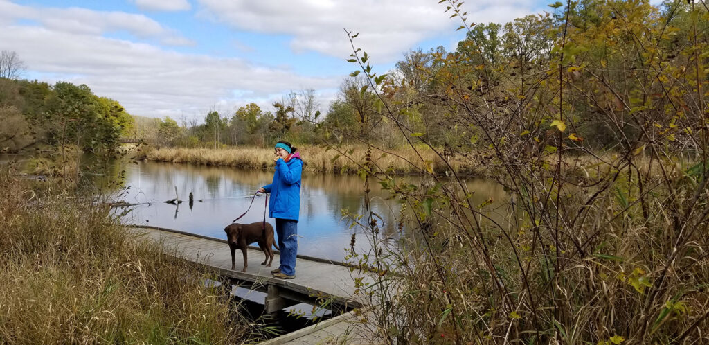 Linda takes her mom's chocolate lab on a walk as she eats an apple along the Kalamazoo River Trail at the Whitehouse Nature Center