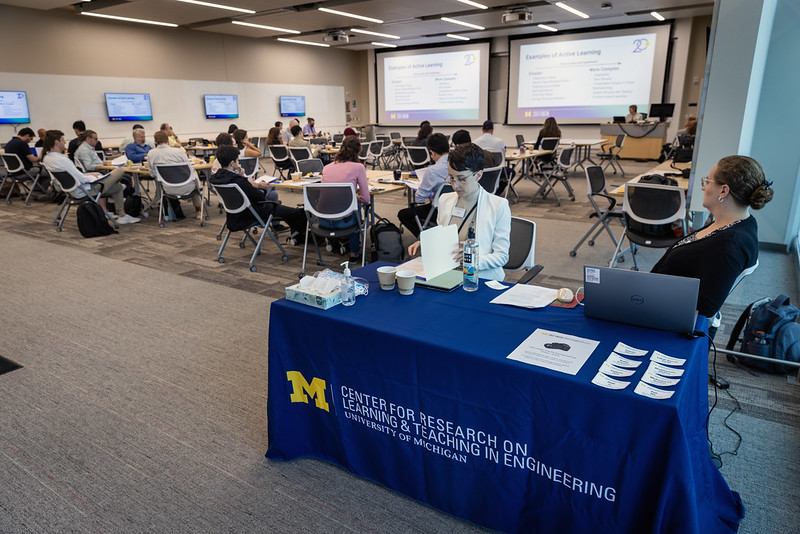 Two women sit at the welcome table for the Michigan Engineering New Faculty Orientation inside a large classroom