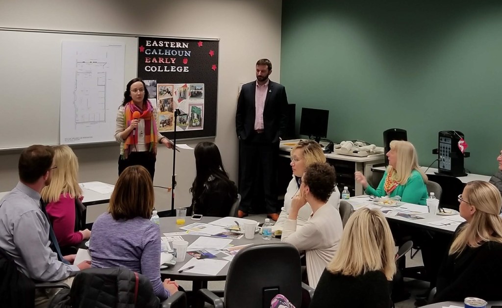 Linda LaNoue speaks into a microphone with a room full of people in the foreground